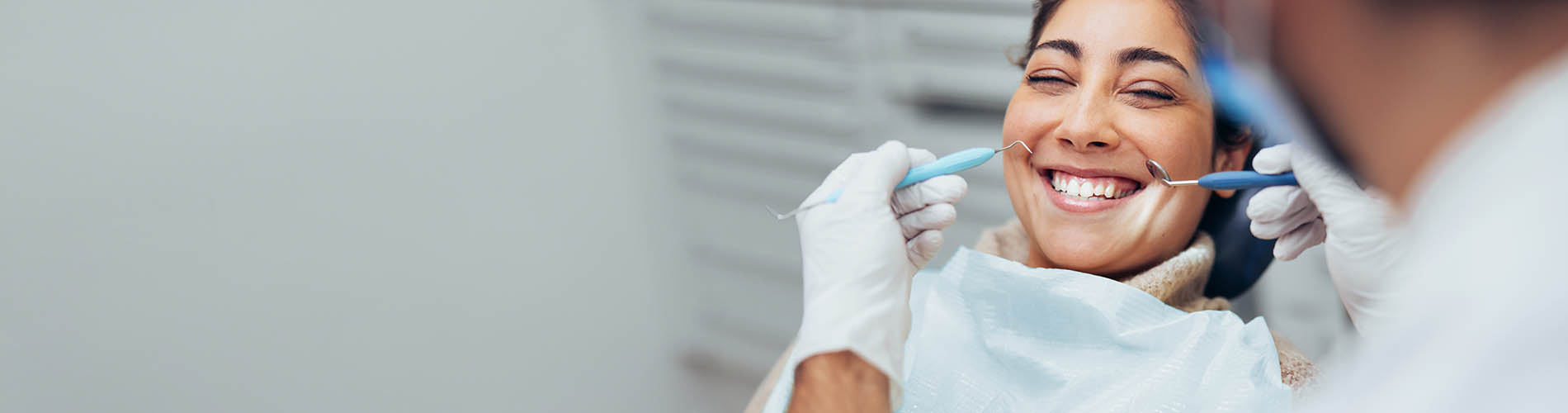 A person is seated in a dental chair, receiving care from a dental professional who stands behind them.